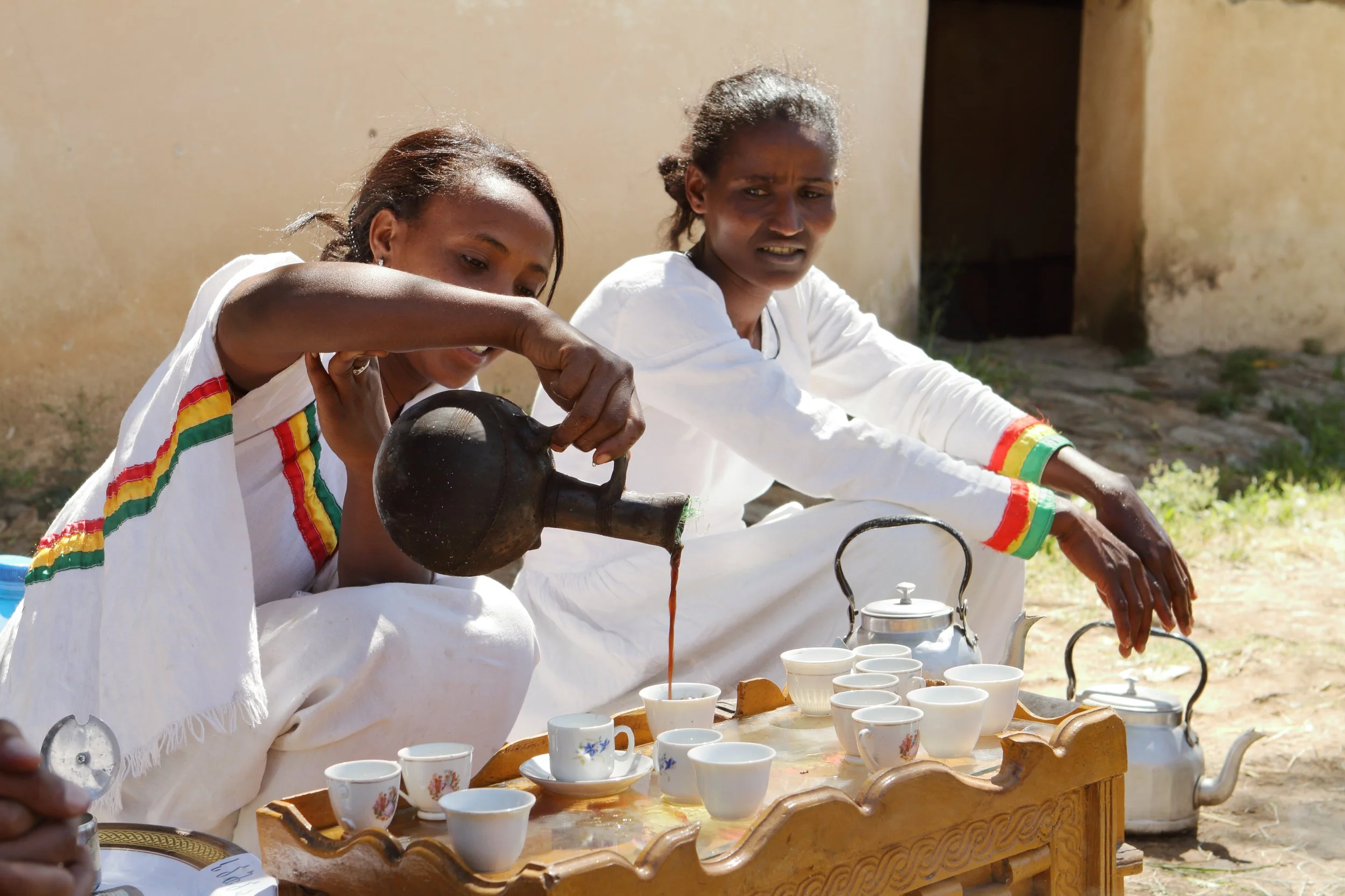 Ethiopian women in traditional dress pouring coffee from a jebena during a traditional coffee ceremony